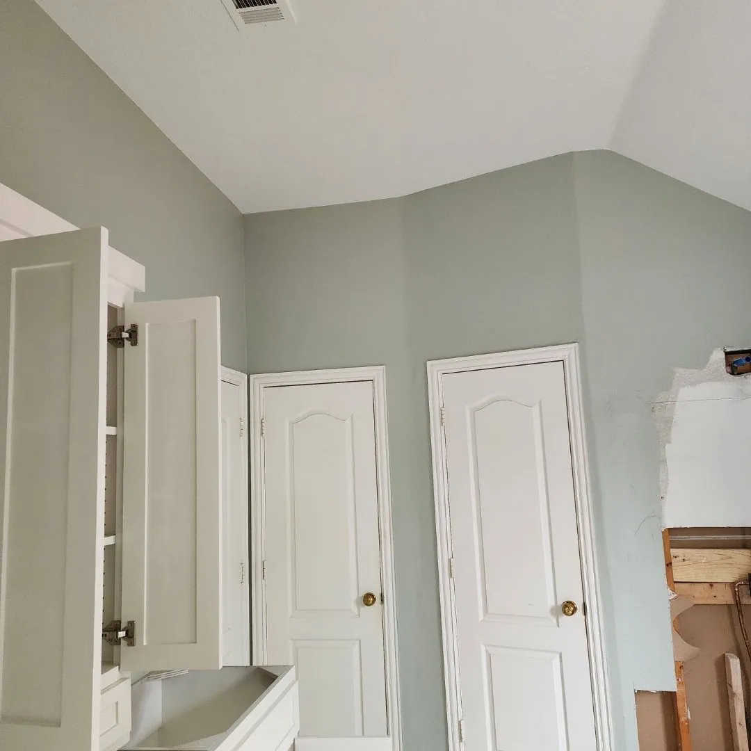 Bathroom remodel in progress with freshly painted walls, new white cabinetry, and one wall opened up to the framing