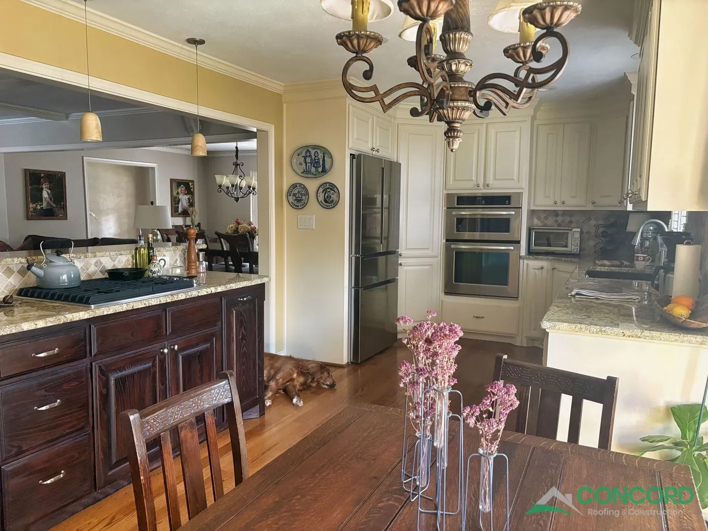 Finished kitchen remodel by Concord Roofing & Construction with cream cabinets, granite countertops, and stainless appliances