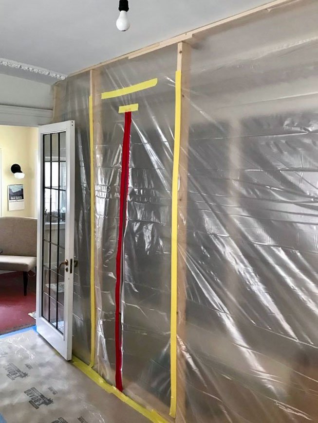 Plastic dust barrier wall with a zippered door sealing off a remodel work area, with floor protection on the floor