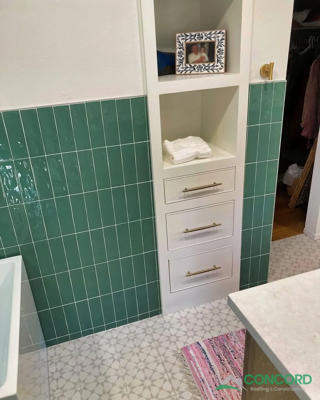 Green tile bathtub wall beside new built-in white storage shelves and drawers in a remodeled Dallas, TX bathroom