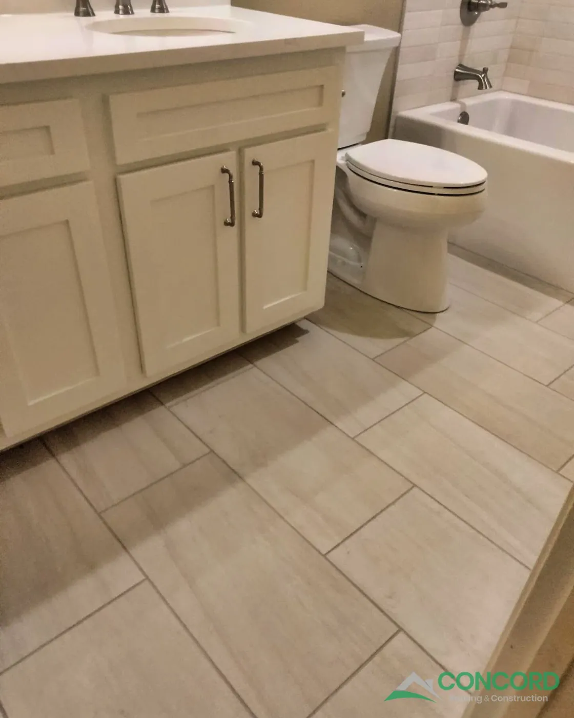 New white vanity with a countertop, a new toilet, and large-format tile flooring next to the new tub in a remodeled Dallas, TX hall bathroom