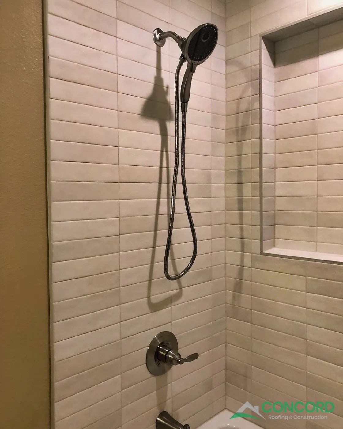New tile surround with a built-in niche and a handheld shower head in a remodeled Dallas, TX hall bathroom