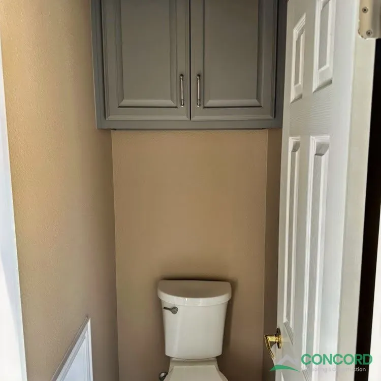 New toilet in the separate toilet room of a remodeled Frisco, TX master bathroom, with a gray cabinet above it