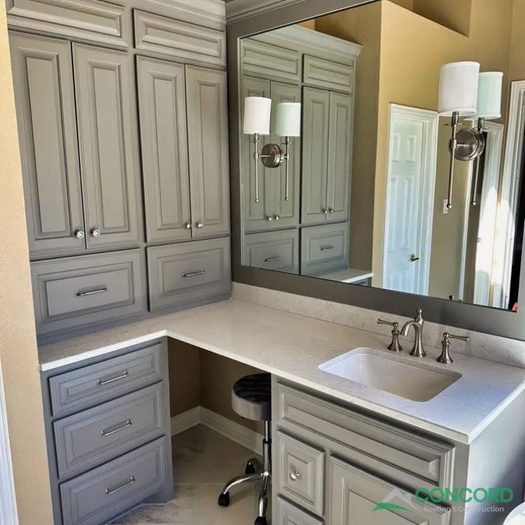 New gray vanity with a white countertop, a seated makeup area, tall cabinets, wall sconces, and a large mirror in a remodeled Frisco, TX master bathroom