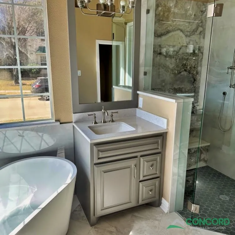 New gray vanity with a white countertop beside a freestanding tub and a glass shower in a remodeled Frisco, TX master bathroom