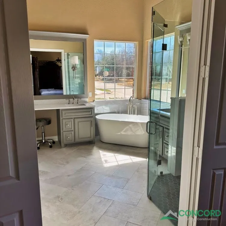 View into a remodeled Frisco, TX master bathroom with new tile flooring, a vanity with a makeup area, a freestanding tub, and a glass shower