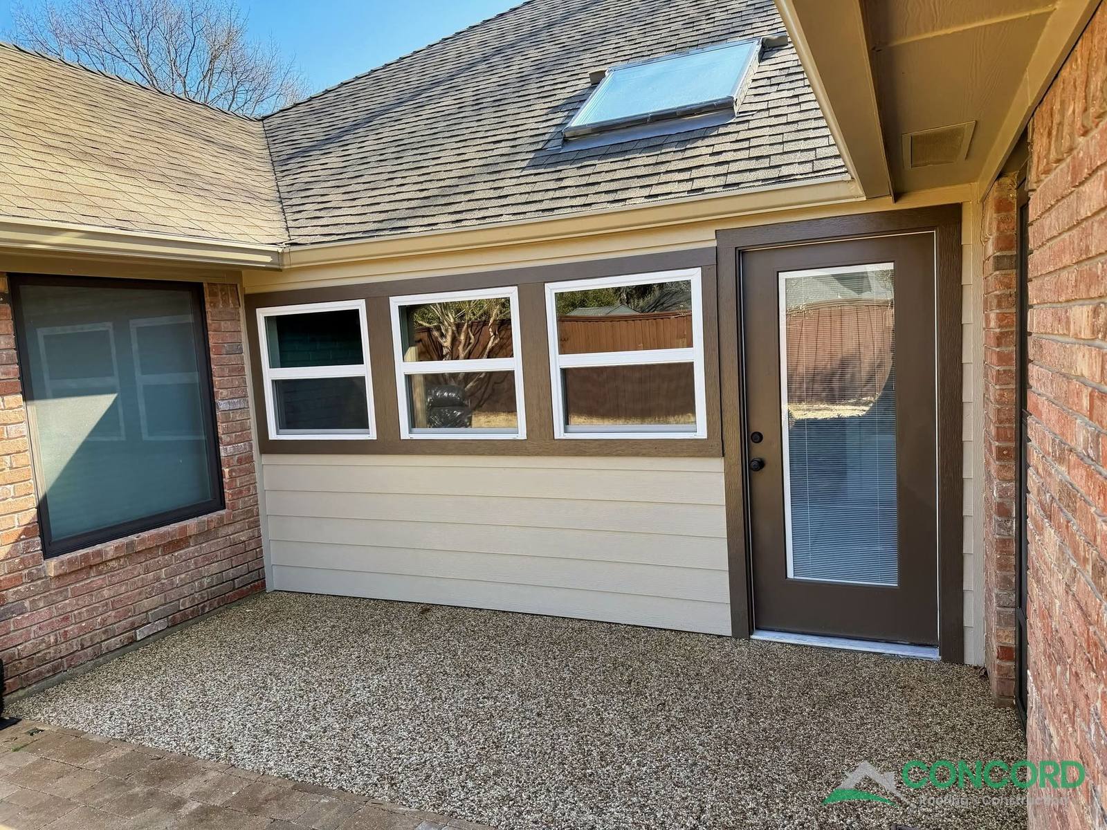 Enclosed patio exterior with three new windows, a full-lite door, lap siding, and a skylight in the roof