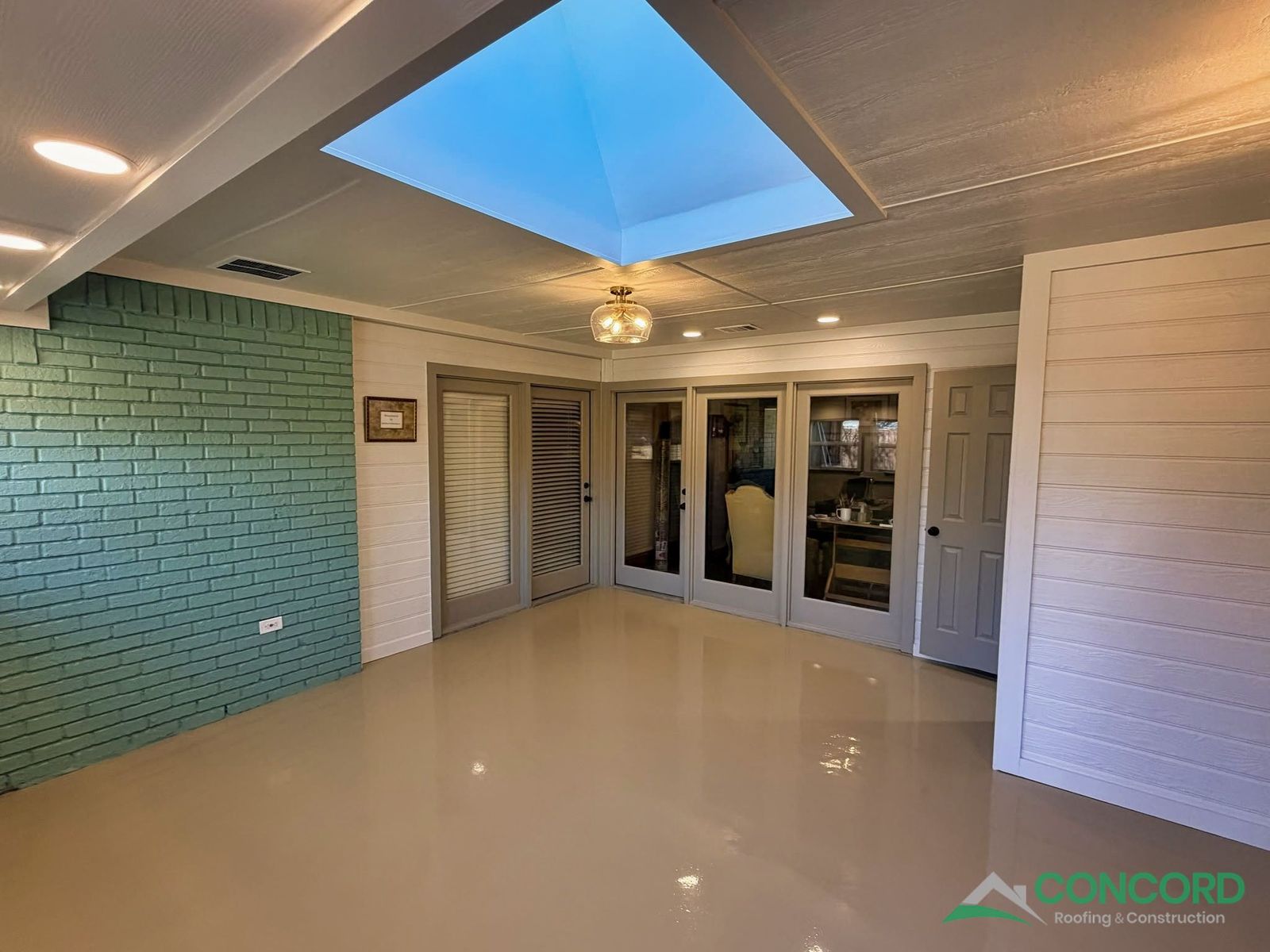 Enclosed patio interior with a skylight, recessed lighting, a painted teal brick accent wall, and an epoxy-coated floor