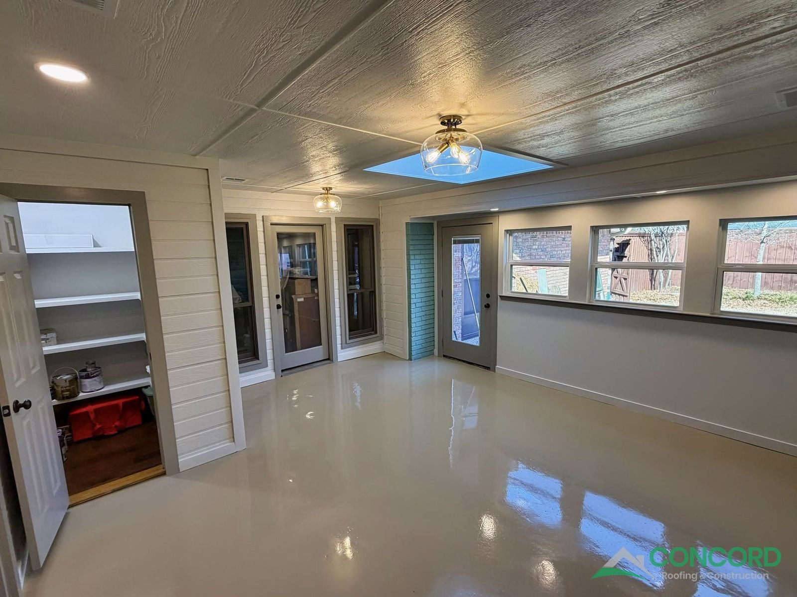 Enclosed patio interior showing new windows, a full-lite door, a built-in storage closet, and a glossy epoxy floor