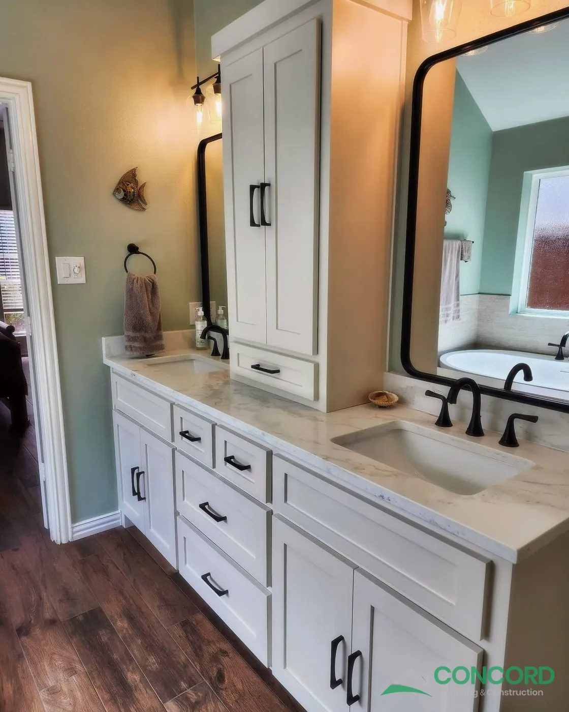 Remodeled McKinney, TX master bathroom with a white double vanity, black fixtures and mirrors, sage green paint, and wood-look tile flooring