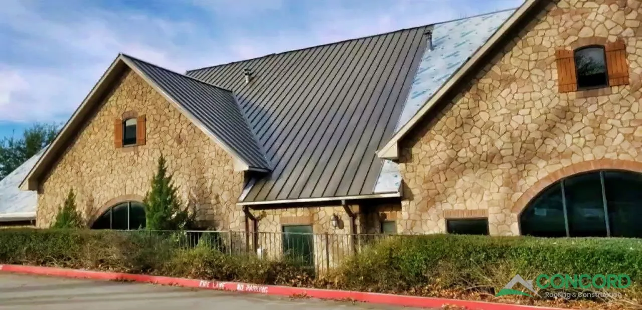 Standing seam metal roof panels being installed over the underlayment on a stone building in McKinney, TX