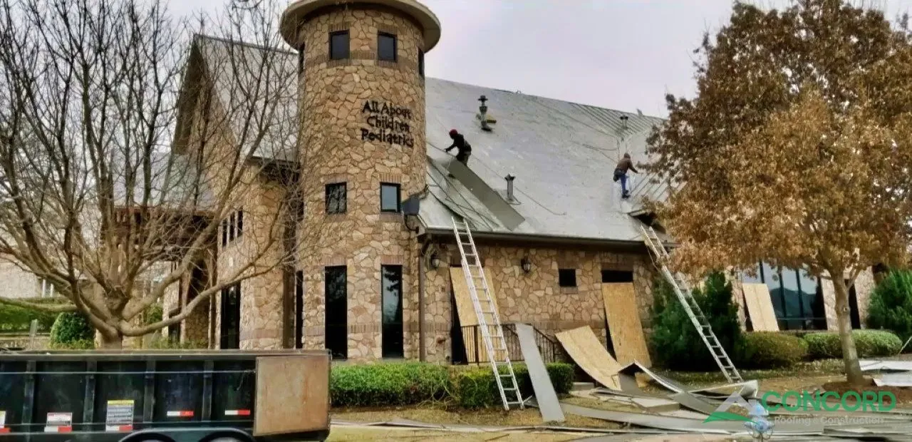 Roofing crew tearing off the old roof beside the All About Children Pediatrics tower in McKinney, TX