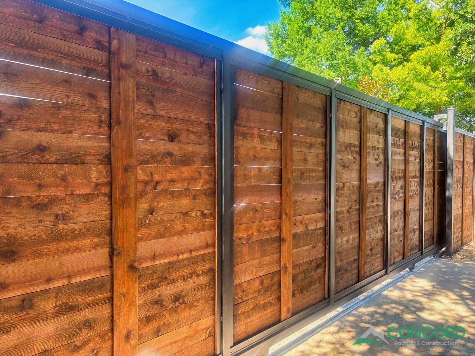 Automatic sliding gate with stained horizontal wood panels in a black steel frame