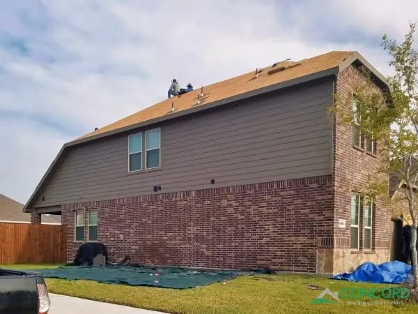 Crew removing the old roof on the back side of a two-story brick home in Princeton, TX, with tarps protecting the yard