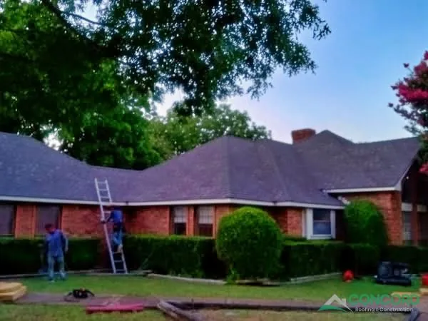 Newly installed roof on the back of a single-story brick home in Waxahachie, TX, with a worker on a ladder at the eave