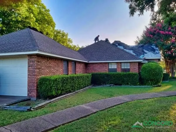 Crew on the roof of a single-story brick home in Waxahachie, TX, with new shingles installed on most of the roof and the last section still being finished