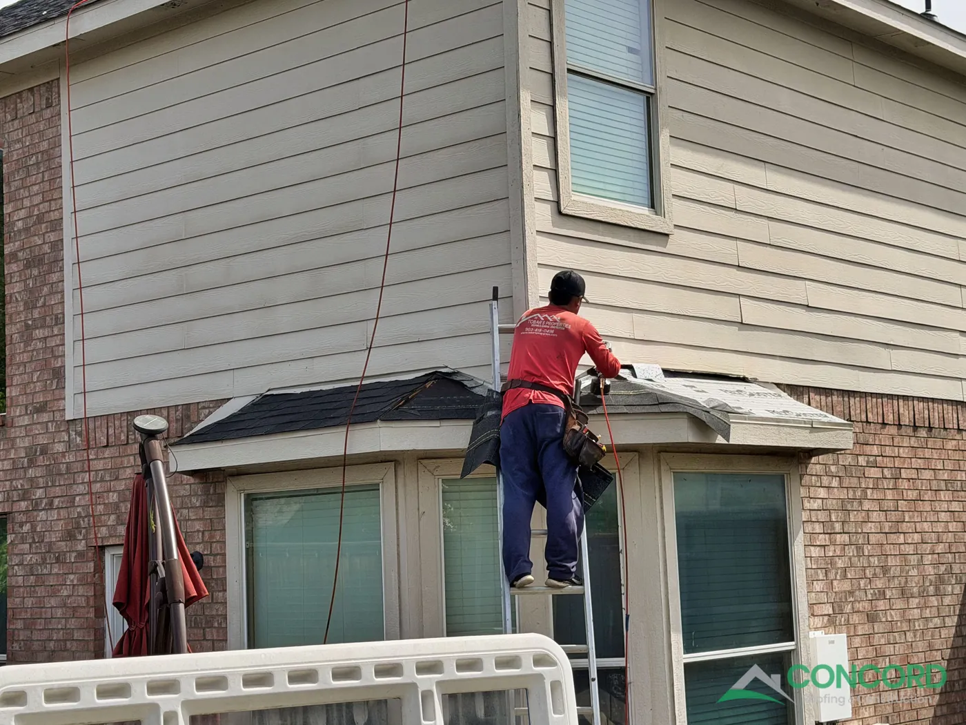 Roofer installing new shingles on a small eave over a bay window of a brick home in Wylie, TX
