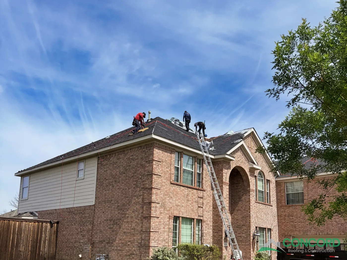 Roofing crew installing new dark impact-resistant shingles on a two-story brick home in Wylie, TX