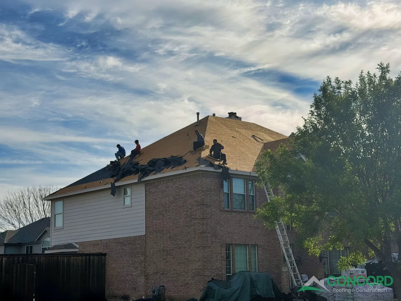 Roofing crew tearing off hail-damaged shingles and underlayment down to the decking on a two-story brick home in Wylie, TX