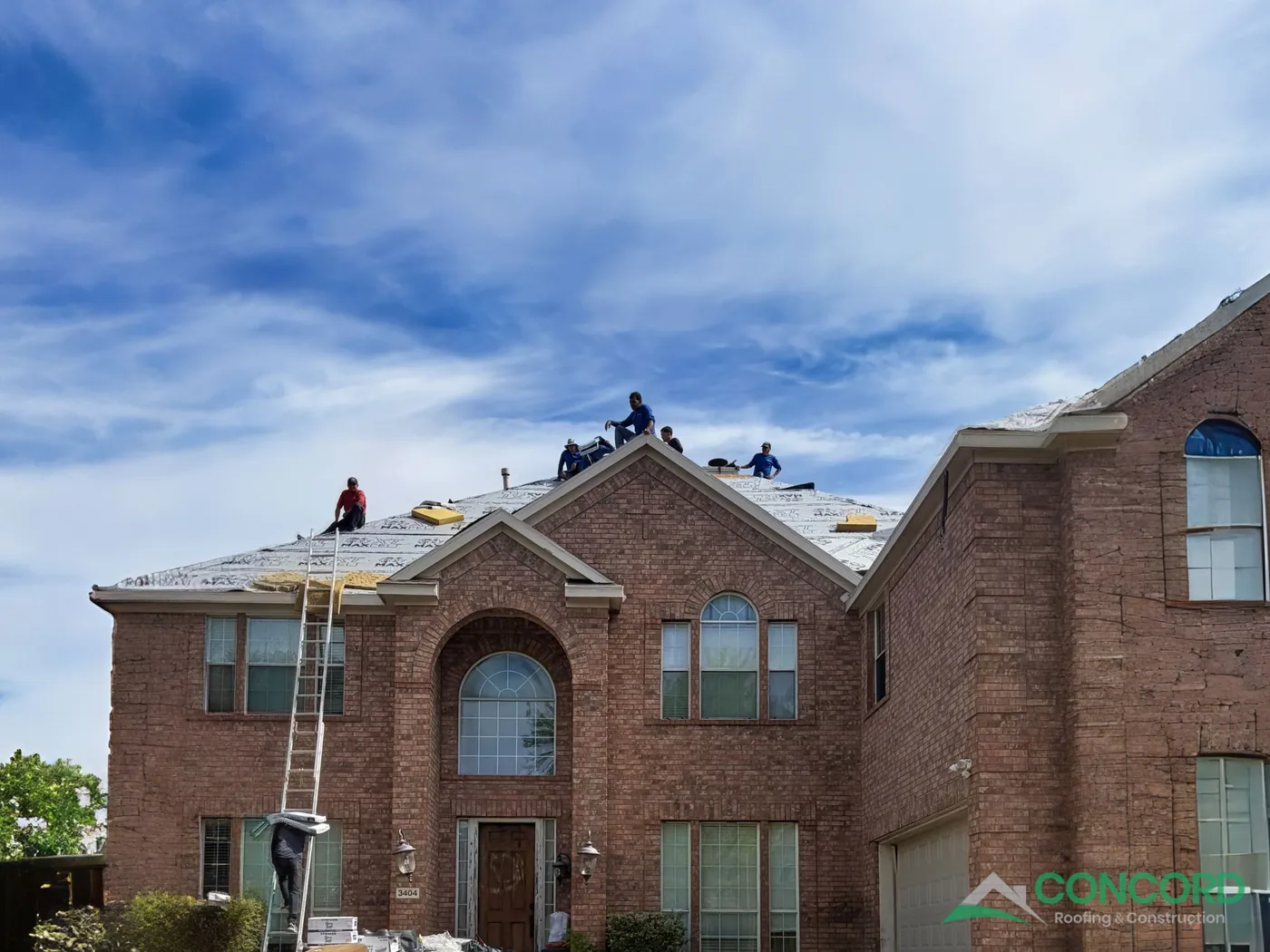 New underlayment covering the roof deck of a two-story brick home in Wylie, TX, with shingle bundles staged on the roof